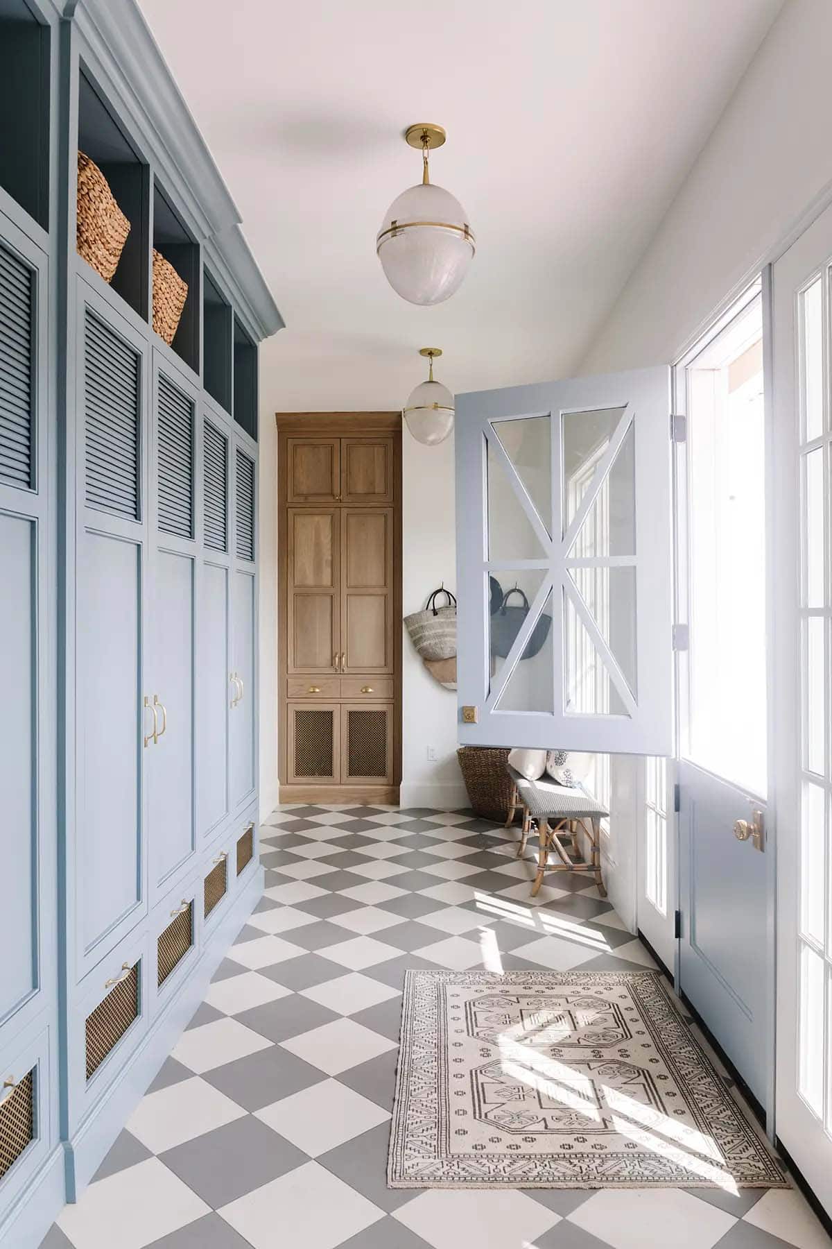 Blue mudroom with checkered tile floor, globe pendant light, and wood storage armoire