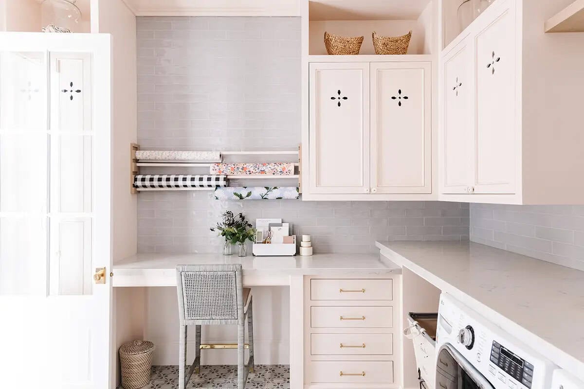 Laundry room craft nook with wrapping paper rack, cane chair, pink cabinets, and gray tile