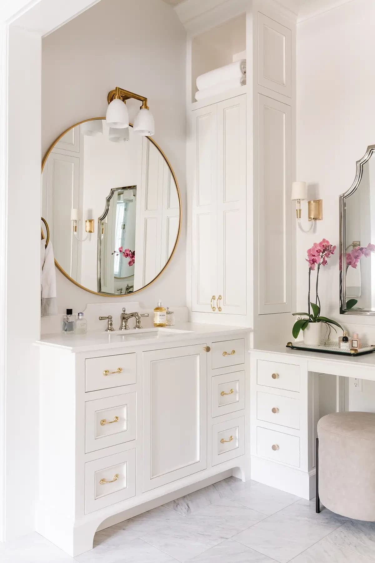 Primary bathroom vanity with round gold mirror, brass hardware, tower cabinet, and orchid
