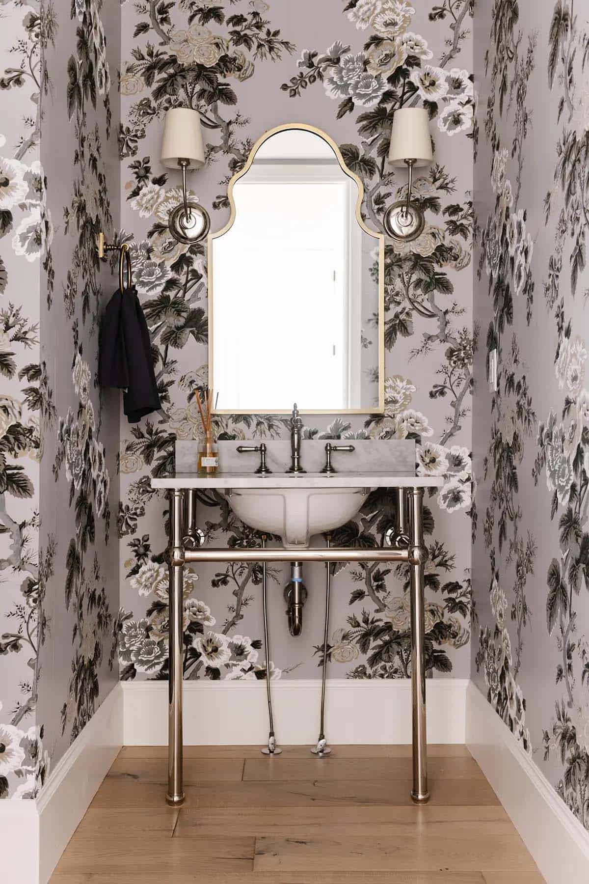Powder room with bold black floral wallpaper, chrome console sink, and arched gold mirror