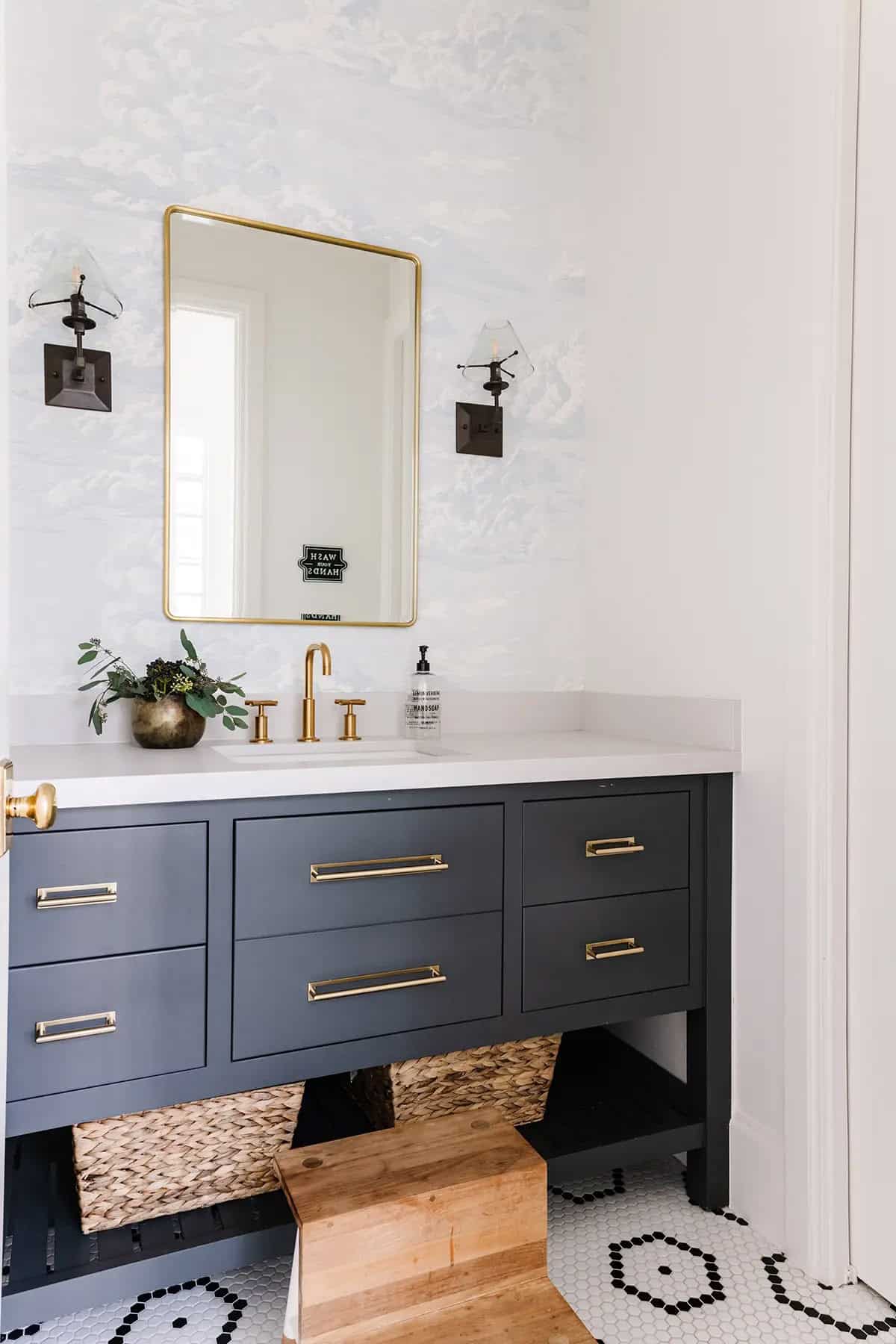Kids bathroom with navy vanity, gold faucet, blue toile wallpaper, and hex tile floor