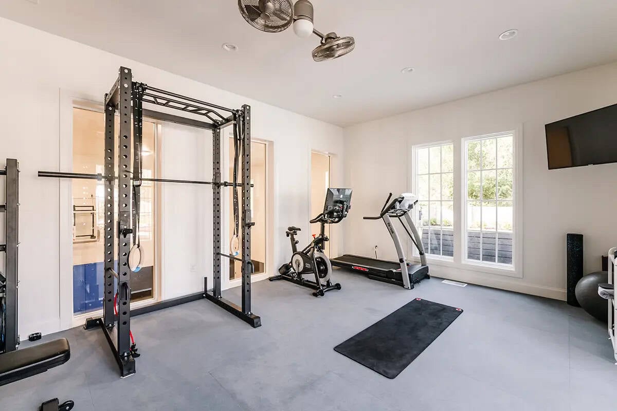 Home gym with power rack, spin bike, treadmill, rubber flooring, and ceiling fan