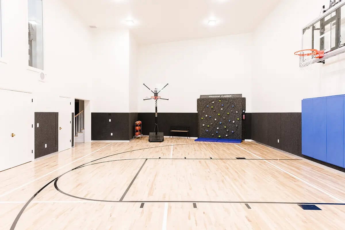 Indoor basketball court with hardwood floor, climbing wall, basketball hoops, and padded walls