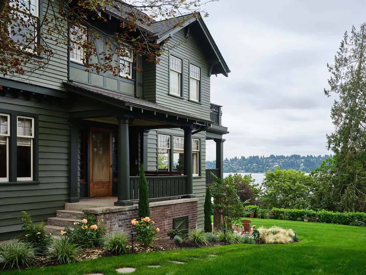 Craftsman farmhouse exterior with sage green siding, covered front porch, brick foundation, and lake views