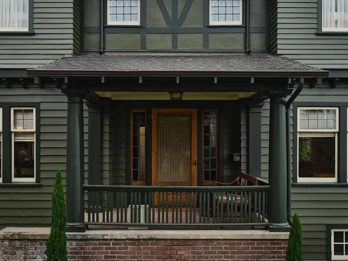 Front entry porch detail with dark green columns, wood door, and Tudor-style upper facade