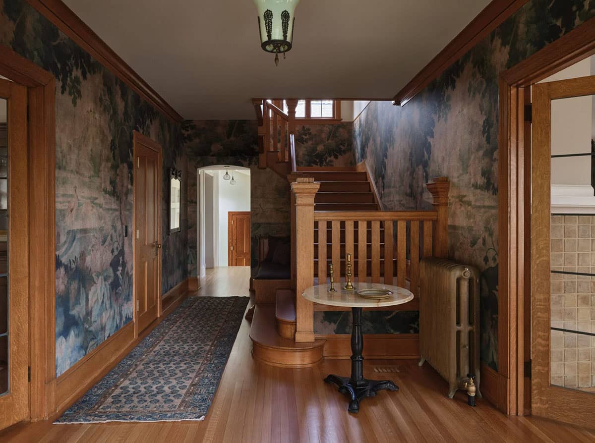 Entryway hall with tapestry wallpaper, oak staircase, hardwood floors, and antique pendant light