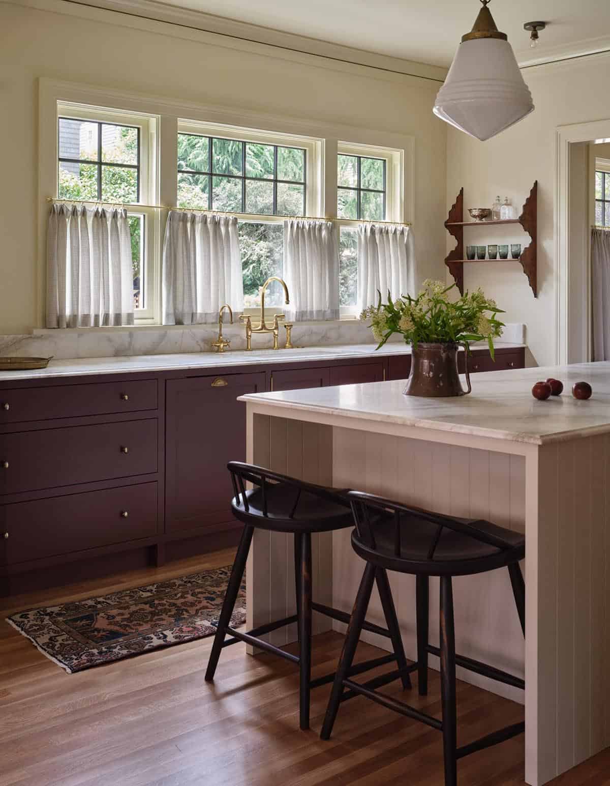 Kitchen with deep plum cabinets, marble countertops, brass bridge faucet, and schoolhouse pendant light