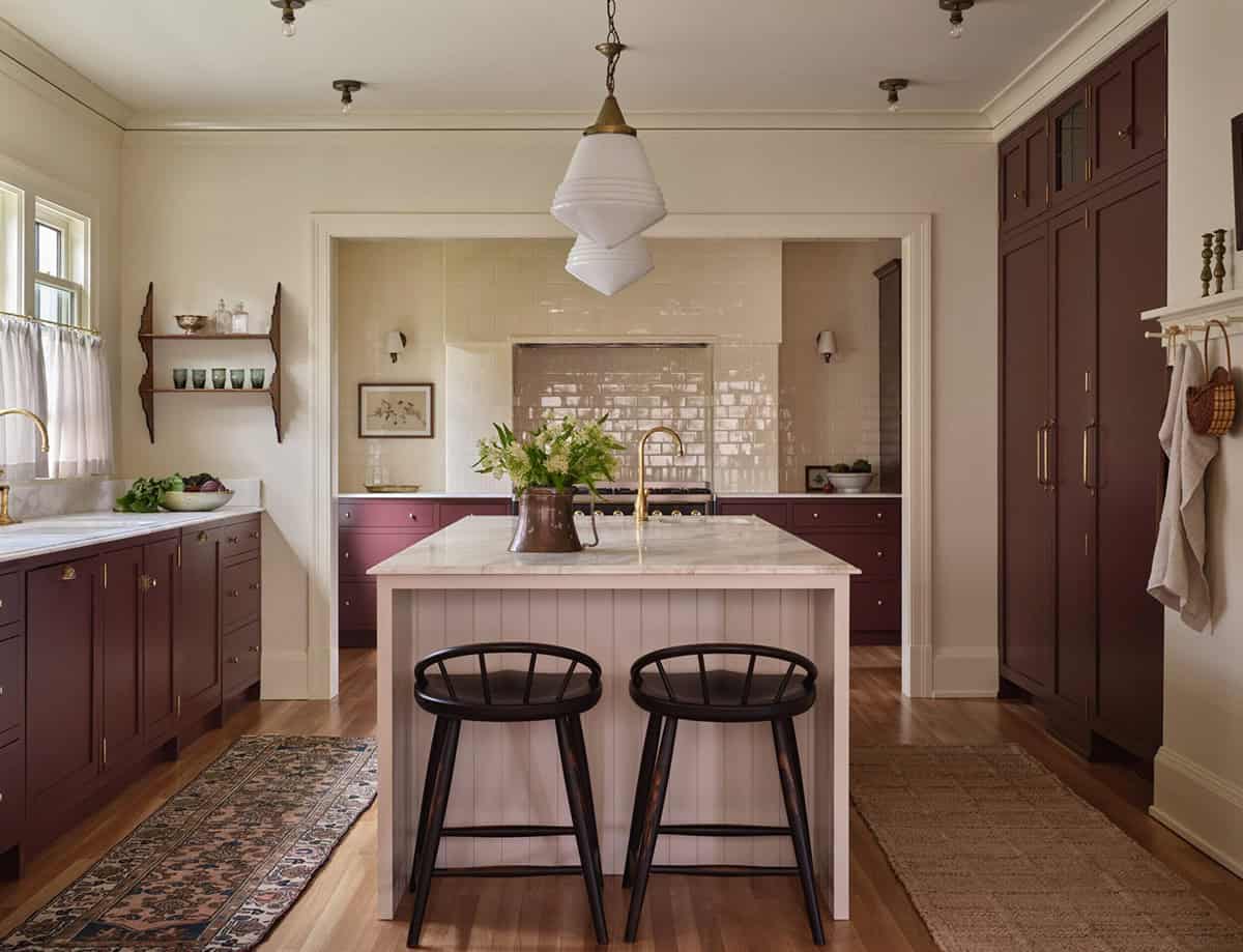 Wide kitchen view showing plum cabinetry, pink island, white tile range alcove, and vintage pendant