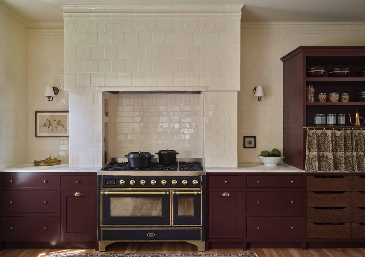 Kitchen range wall with cream subway tile, tiled hood, black and brass range, and open shelving
