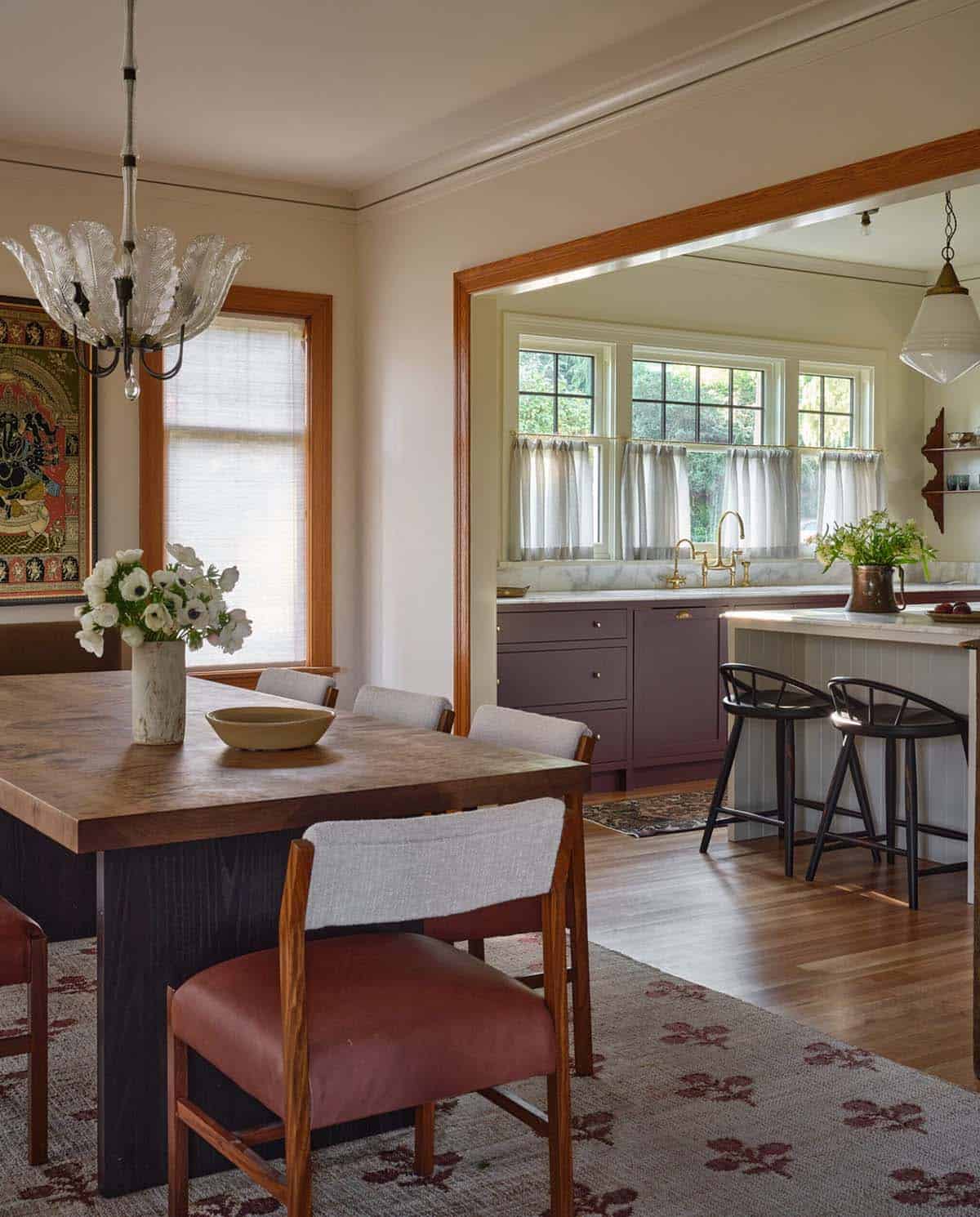 Dining room open to kitchen with wood table, rust chairs, glass chandelier, and warm-toned rugs