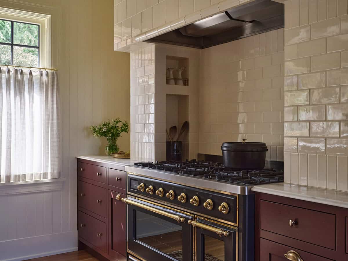 Close-up of black and brass range with cream zellige tile backsplash and plum lower cabinets