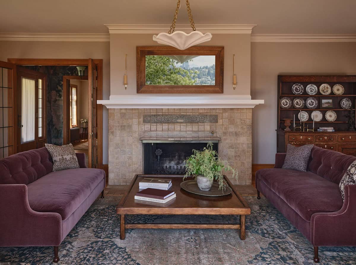 Living room with plum velvet sofas, tile fireplace, wood mirror, and antique hutch