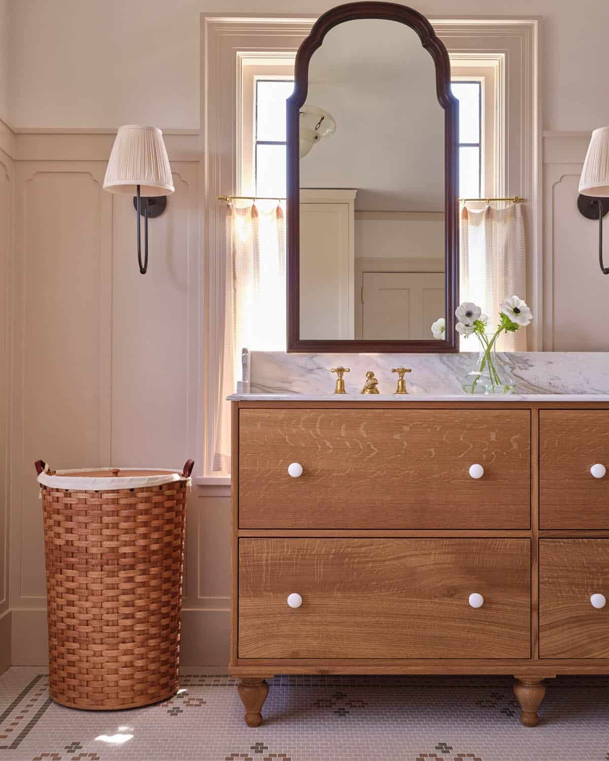 Bathroom vanity with oak dresser base, arched wood mirror, marble top, and brass faucet