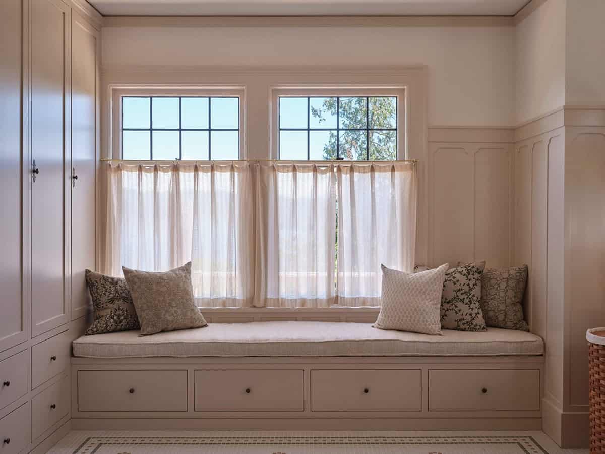 Built-in window seat with storage drawers, patterned cushions, and sheer cafe curtains