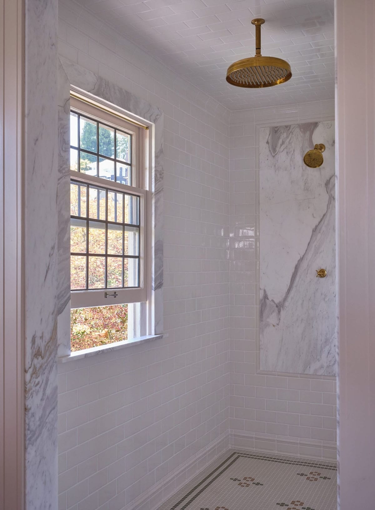 Walk-in shower with white subway tile, dramatic marble slab, brass rain head, and garden window