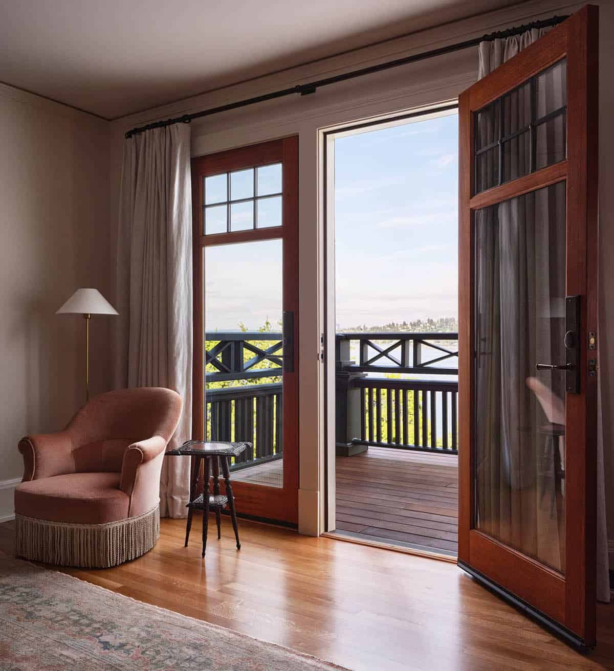 Bedroom corner with pink velvet chair, open French doors to lake-view balcony, and hardwood floors