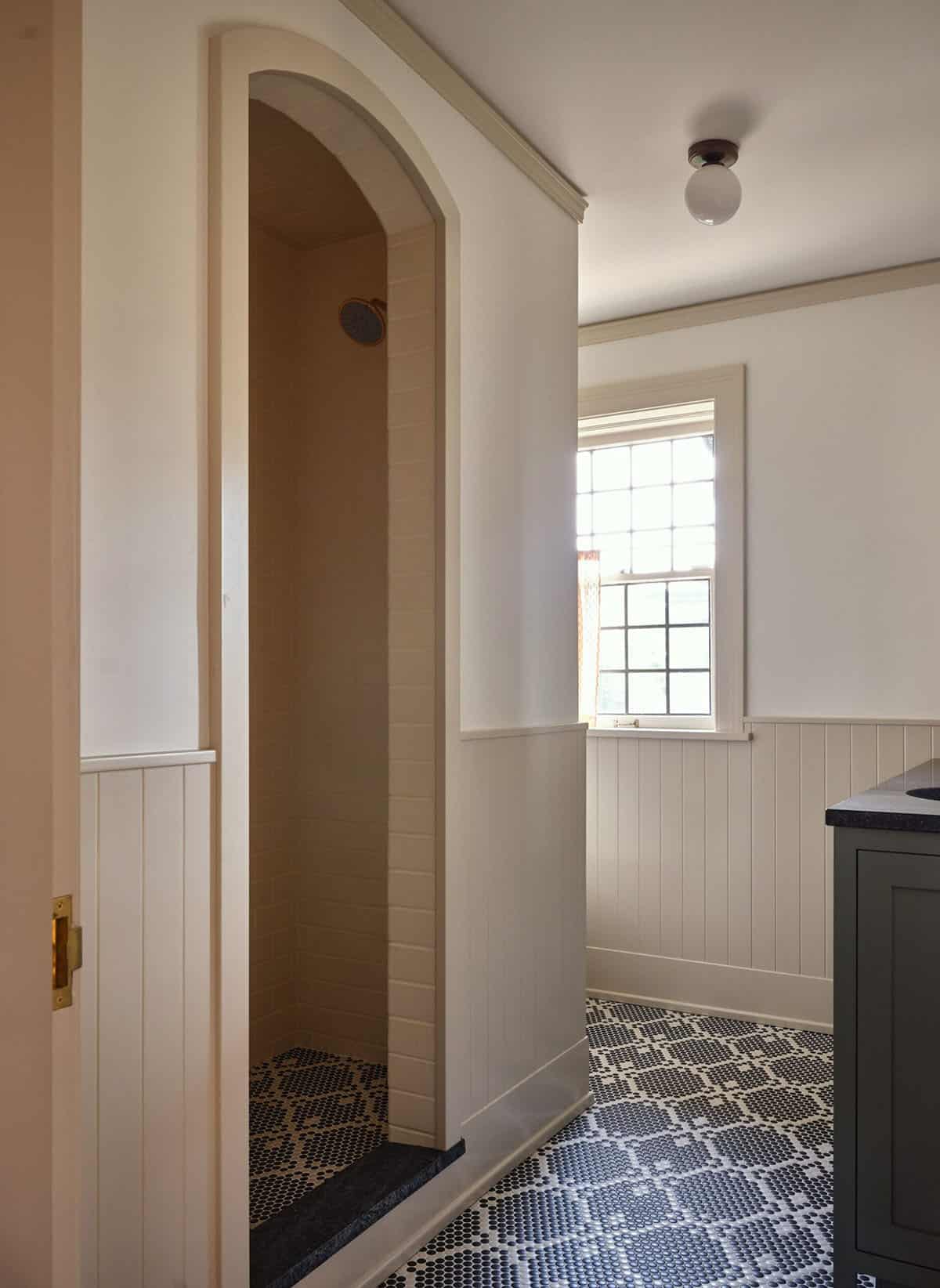 Bathroom with arched shower entry, black and white penny tile floor, and globe ceiling light