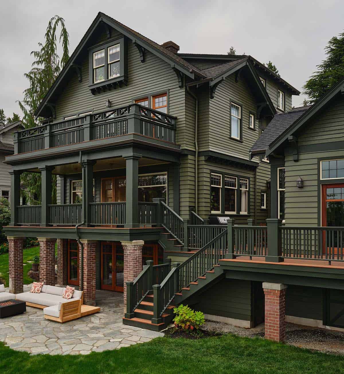 Angled rear view of green craftsman home with stacked porches, brick piers, and wood stair railings