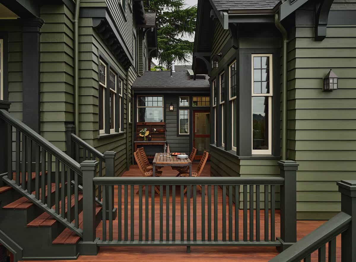 Covered deck with wood dining set between green craftsman buildings and garden lantern