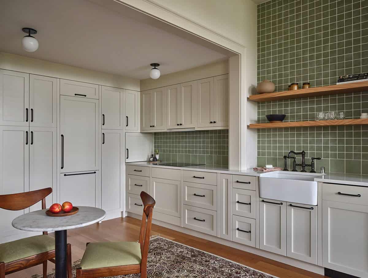 Cottage kitchen with white cabinetry, sage green tile, apron sink, and marble bistro table