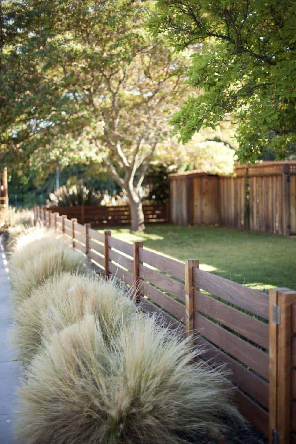 Narrow garden bed along a horizontal wood fence planted with Mexican feather grass