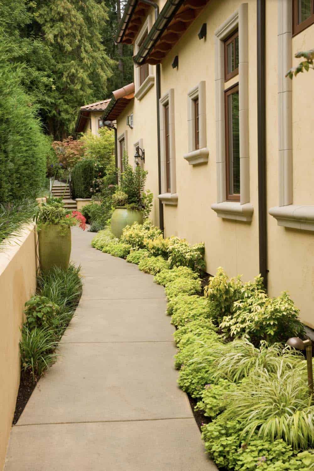 Narrow side yard path along a stucco home with lush chartreuse plantings and large green ceramic pots