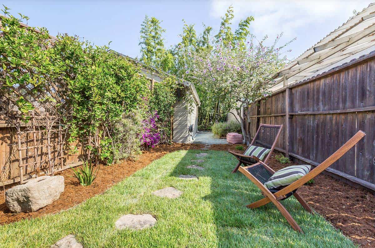 Narrow side yard with lawn, bougainvillea trellis, flowering trees, boulder accents, and lounge chairs