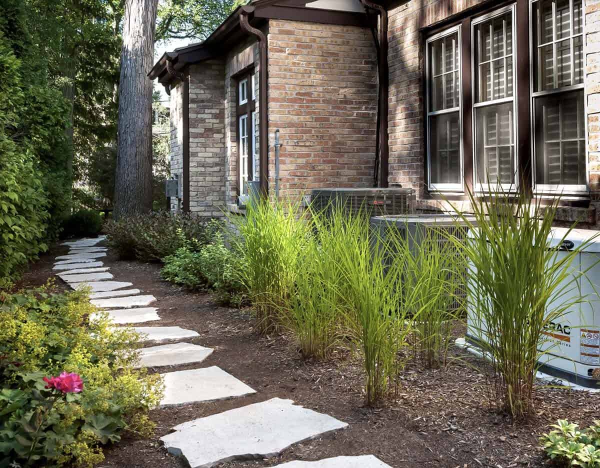 Narrow side yard with flagstone path, ornamental grasses screening AC units, and foundation plantings in Chicago