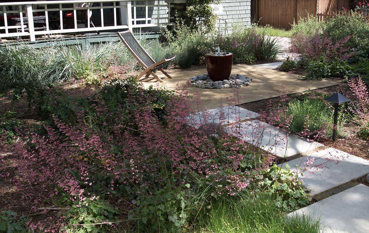 Small front yard with stepping stone path, bubbling fountain, deck chair, and pink flowering ground cover