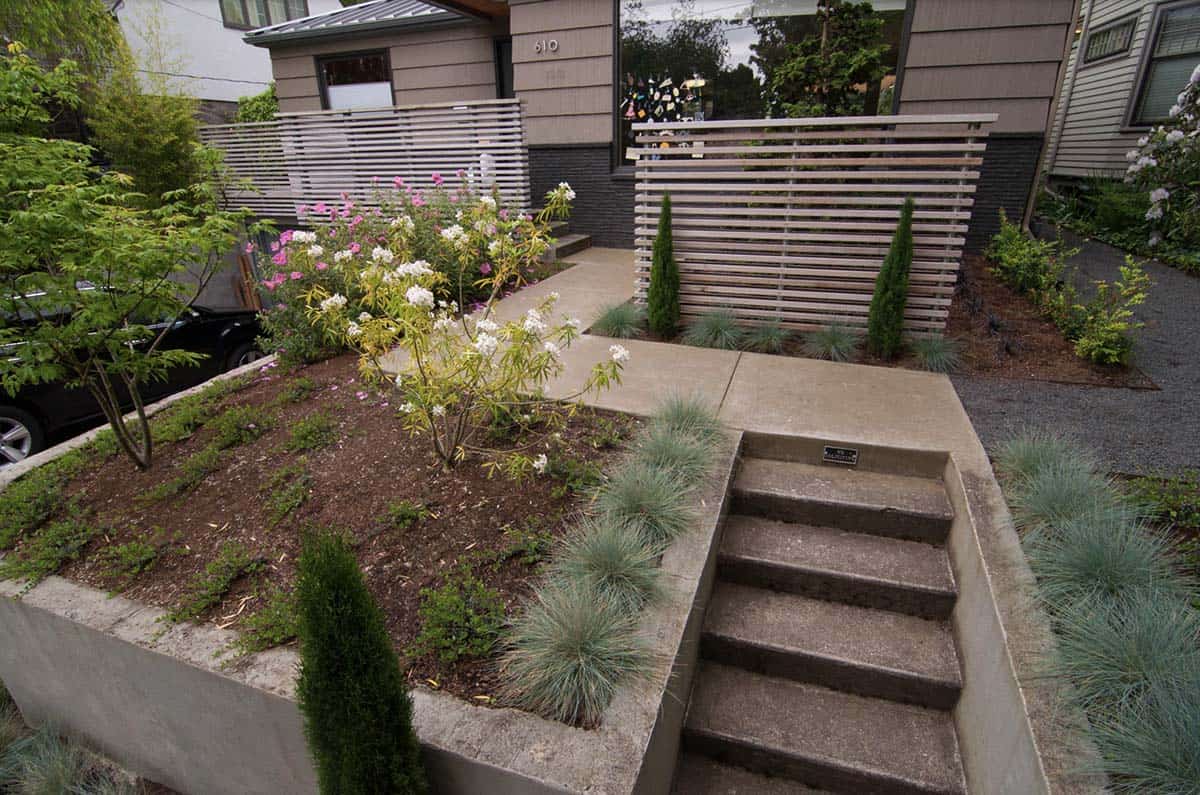 Small front yard with concrete steps, horizontal slat privacy screens, blue fescue, and raised planting bed