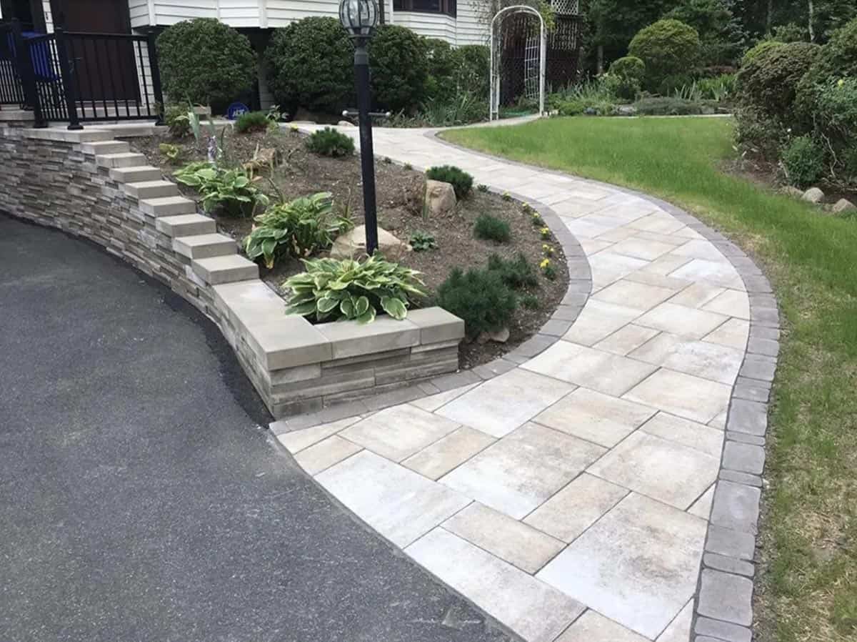 Curved paver walkway with stacked stone retaining wall, raised planting bed, and hostas
