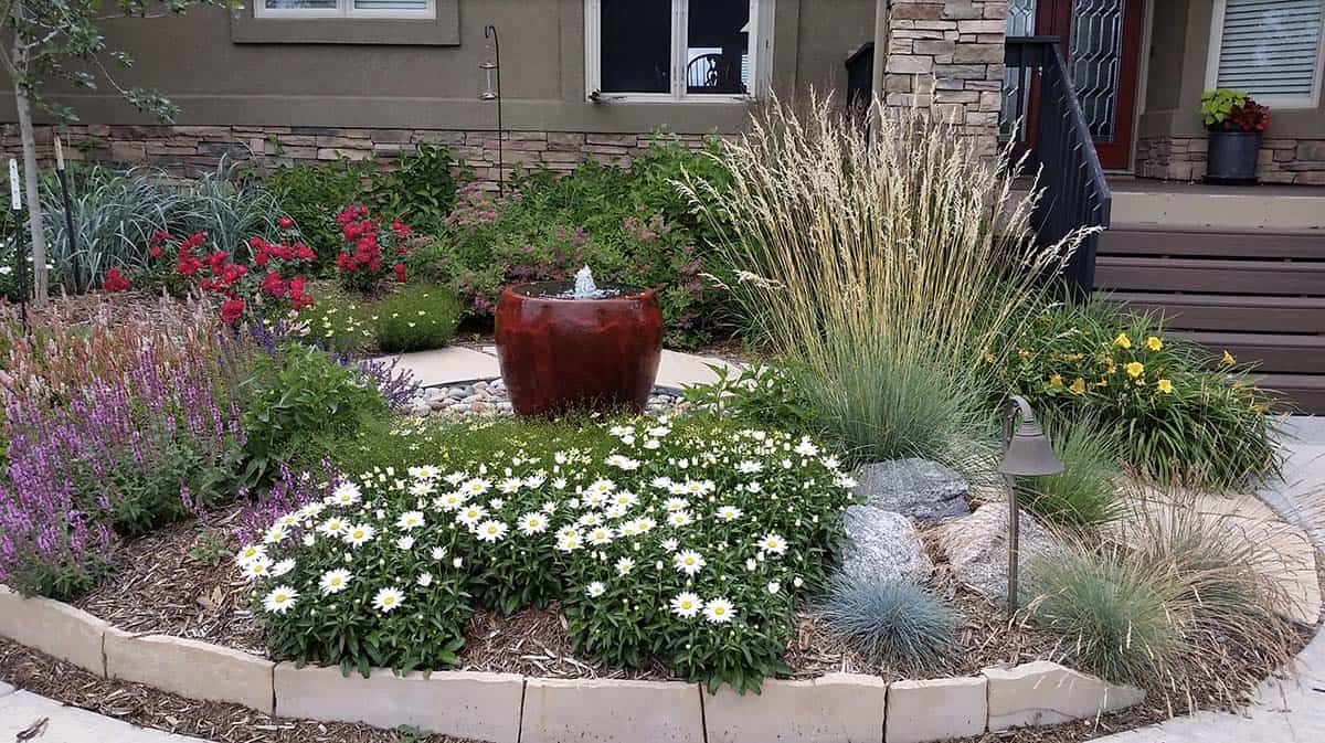 Small front yard garden with ceramic fountain, ornamental grasses, daisies, salvia, and landscape lighting