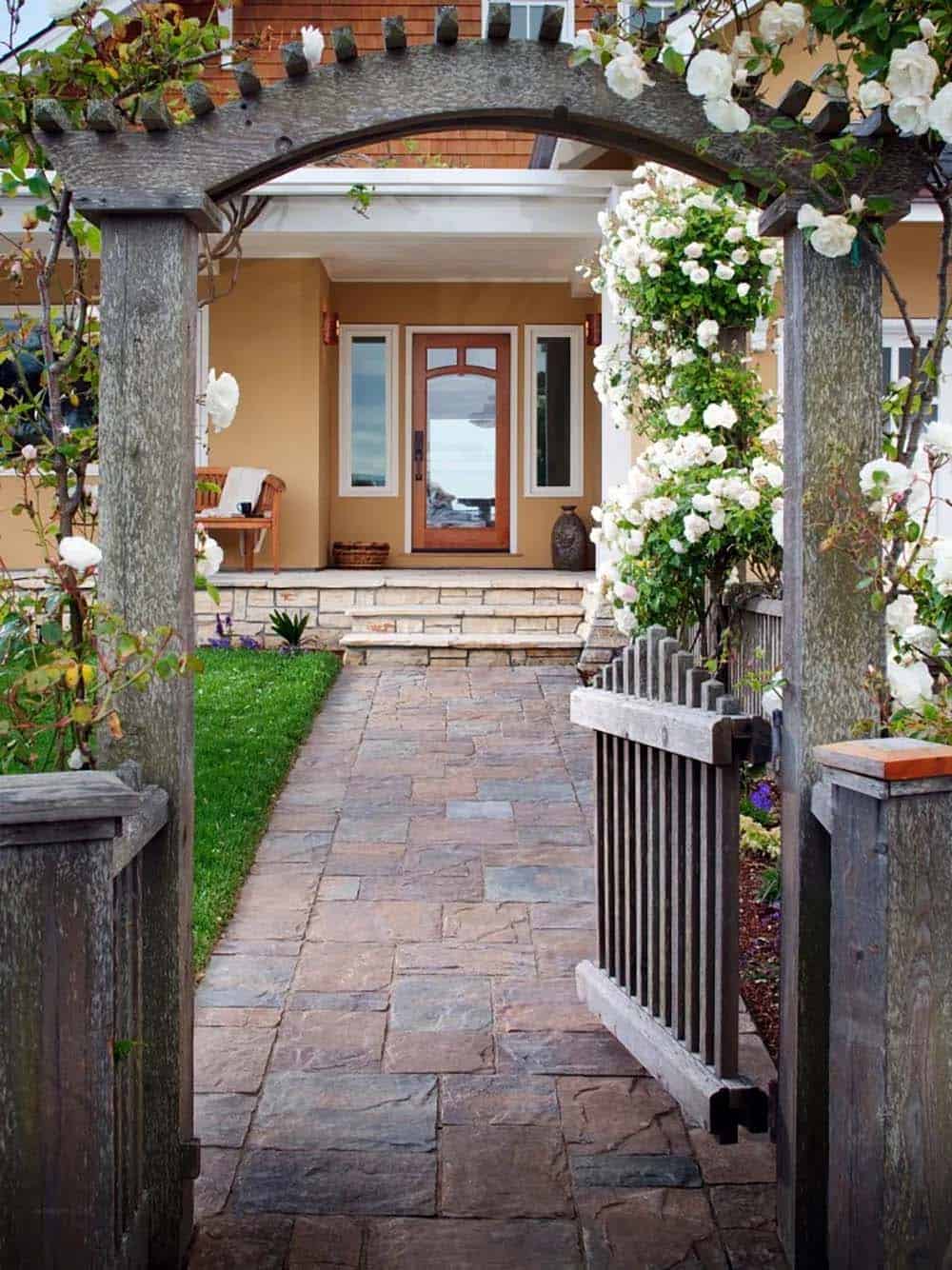 Front yard entry with climbing white roses on wooden arbor, stone paver path, and gate