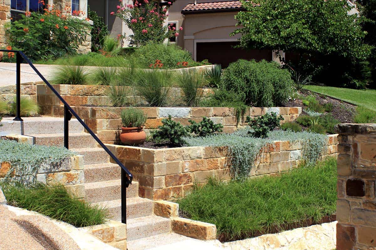 Terraced front yard with limestone retaining walls, ornamental grasses, and custom staircase in Austin Texas