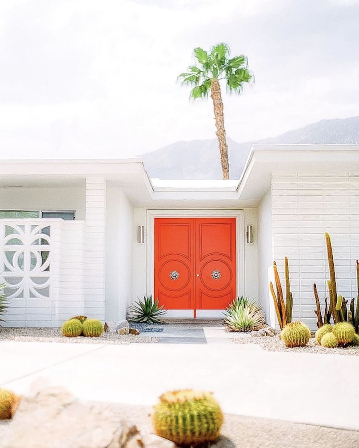 Mid-century modern home with bold orange double doors, gravel, barrel cactus, and agave landscaping
