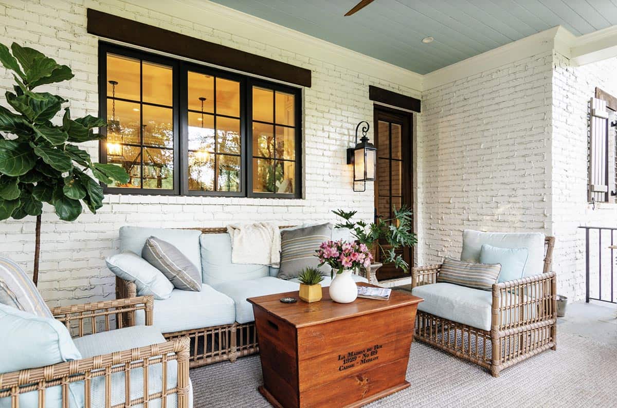 White Brick Porch With Rattan Seating, Vintage Trunk Coffee Table, and Blue Ceiling