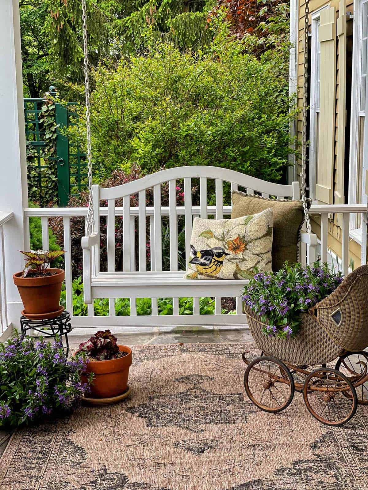 White Porch Swing With Hooked Pillow, Terracotta Pots, and Vintage Wicker Crib
