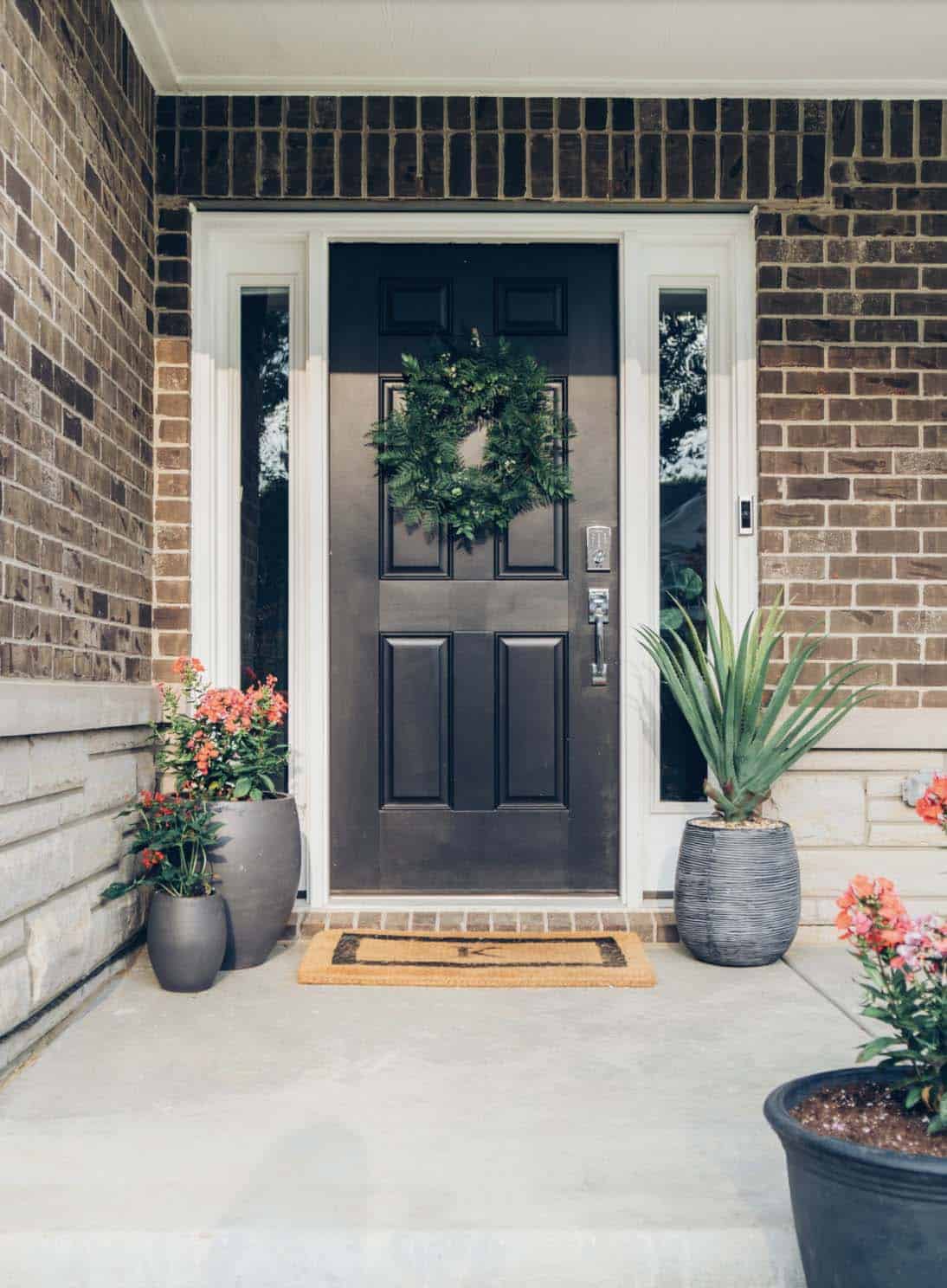 Brick Home Entry With Black Door, Fern Wreath, and Grey Ribbed Planters