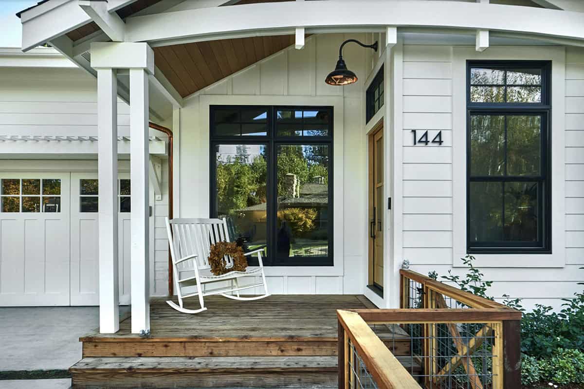 White Farmhouse Porch With Wood Deck, Gooseneck Barn Light, and White Rocking Chair