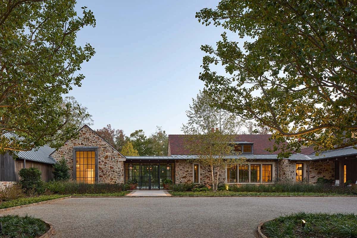 Stone home front facade at dusk with circular driveway, steel windows, and mature trees in Serenbe Georgia