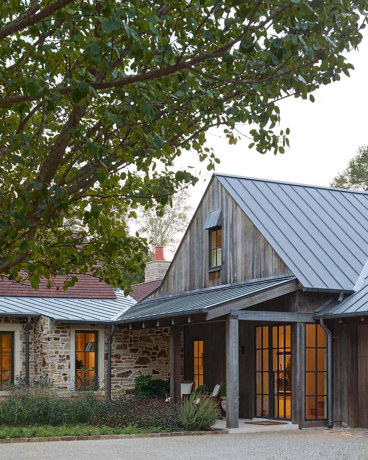 Reclaimed wood barn structure with metal roof and steel French doors framed by trees at dusk