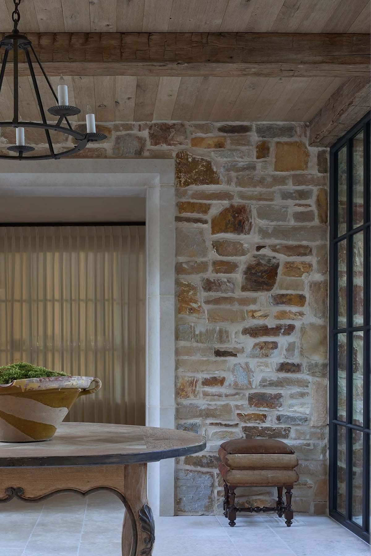 Detail of foyer with antique table, moss bowl, leather stool, and exposed stone wall