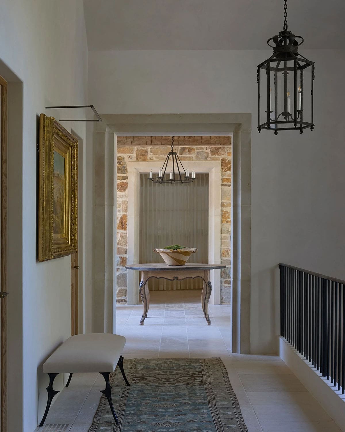  Hallway with iron lantern, gilt-framed painting, upholstered bench, and view into stone foyer