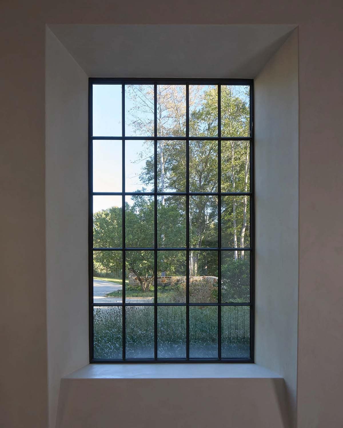 Tall steel-framed window set in plaster wall with garden view beyond
