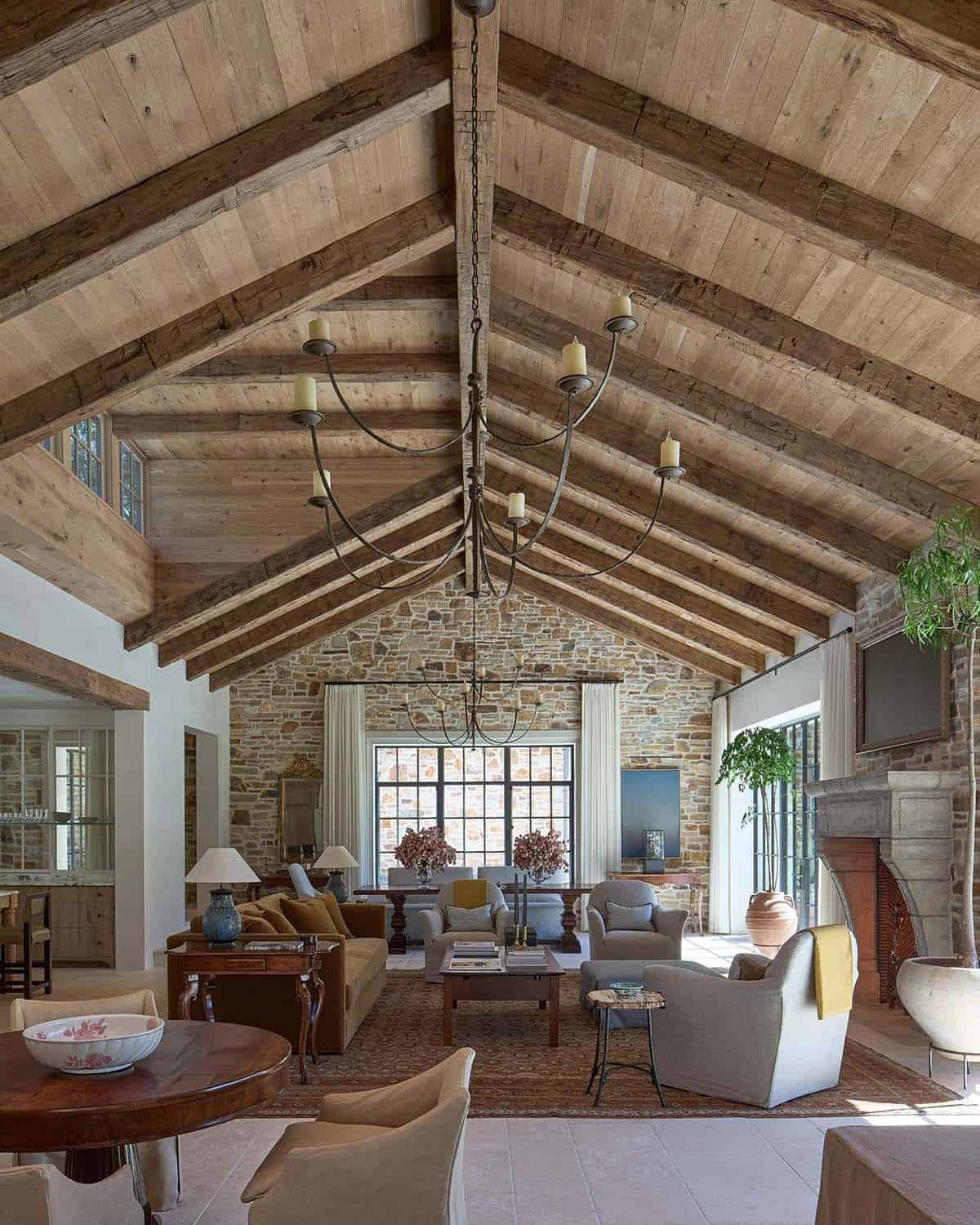 Vaulted great room with reclaimed wood ceiling, exposed beams, iron chandelier, and stone end wall