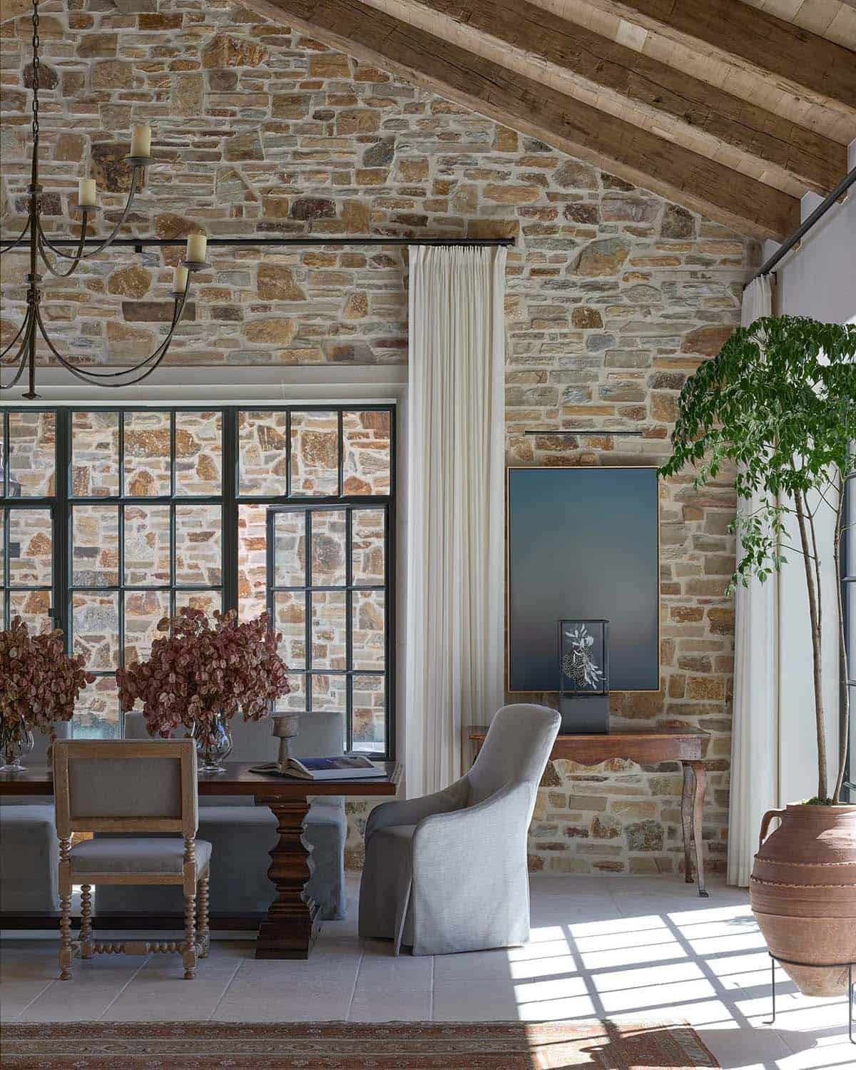 Living area with stone walls, exposed wood beams, steel windows, and mixed antique seating