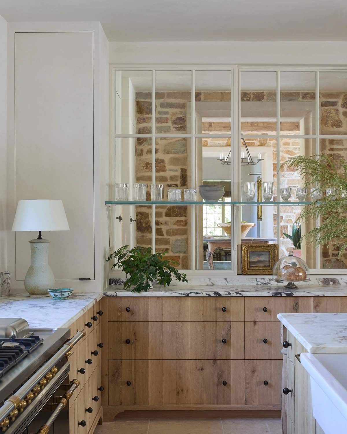 Kitchen with oak cabinetry, marble countertops, steel pass-through window, and French range