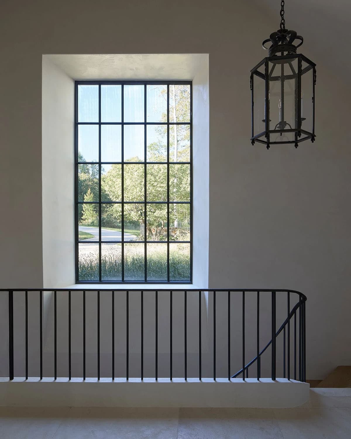 Staircase landing with black iron railing, tall steel-framed window, and iron lantern pendant