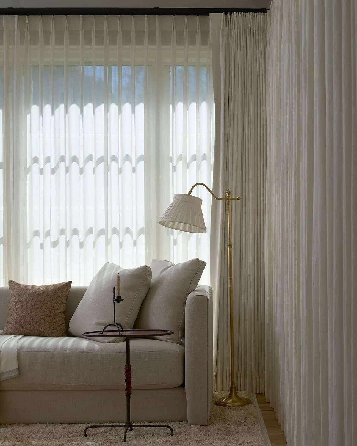 Bedroom sitting area with linen sofa, brass floor lamp, and sheer curtains against steel windows