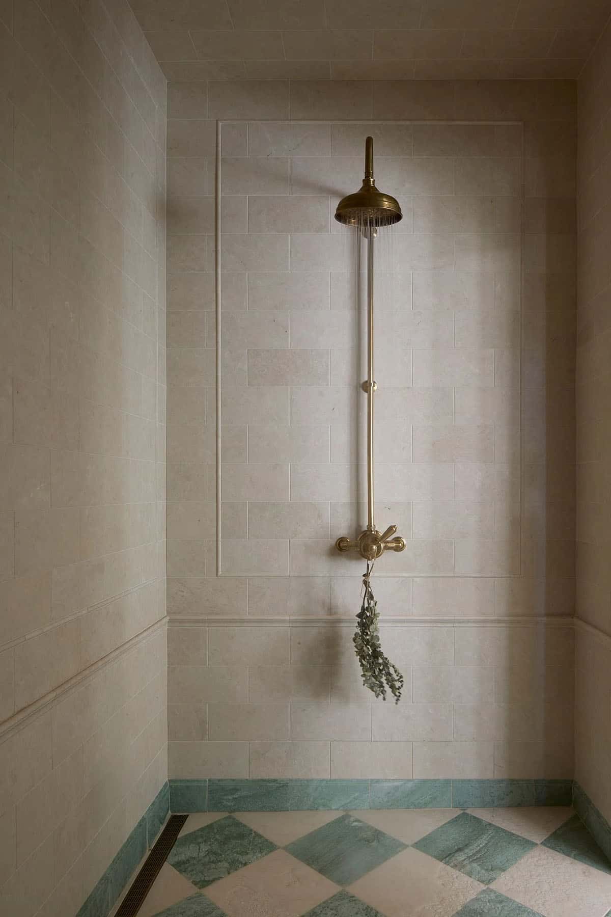 Walk-in shower with stone tile walls, brass rainfall fixture, and green and white checkerboard marble floor